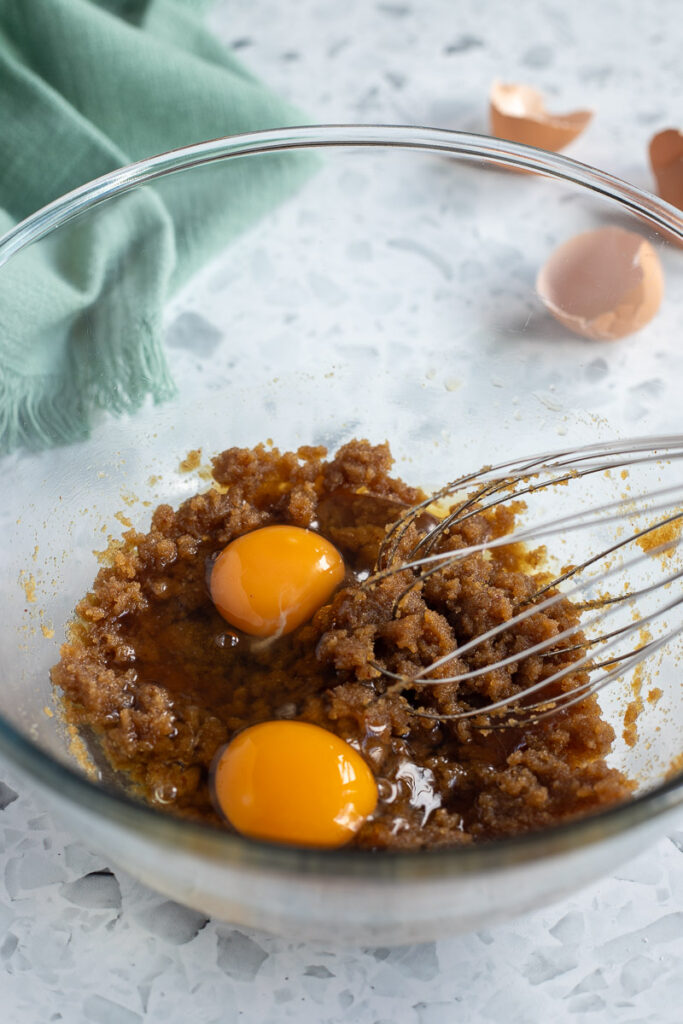 Mixing bowl with cracked eggs added to wet ingredients. Eggshells in the background.