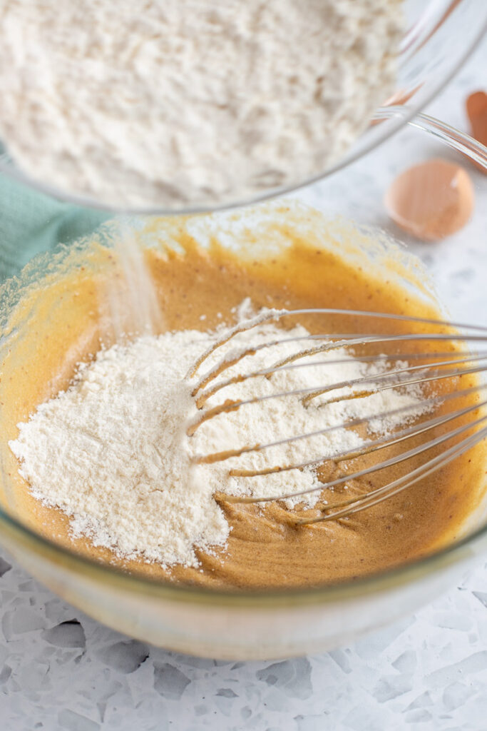 Dry ingredients being poured into a bowl of wet ingredients with a whisk inside.