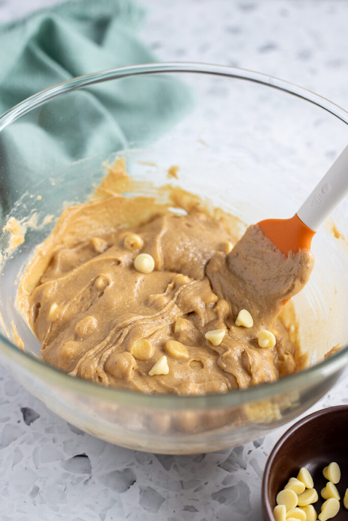 White chocolate chips being folded into blondie batter, with a brown ramekin of chocolate chips in the foreground.