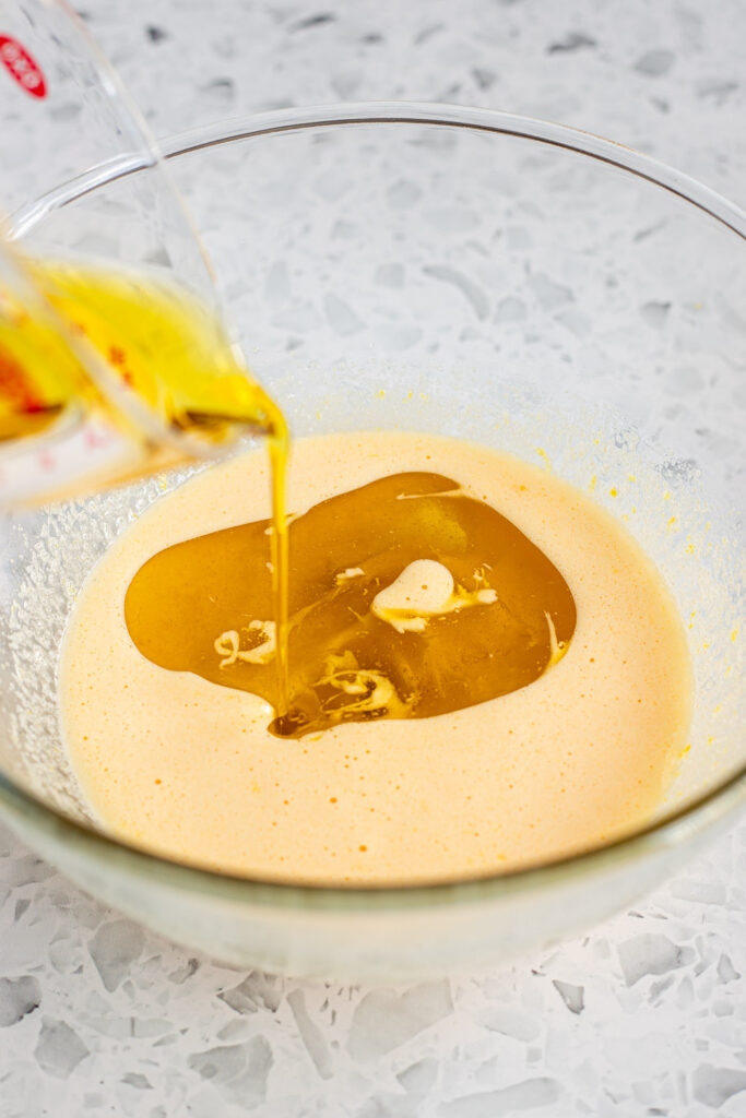 Olive oil being slowly drizzled into cake batter in a mixing bowl.