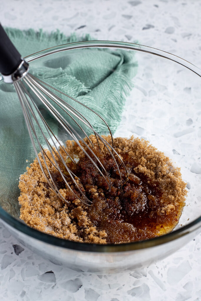 Large glass bowl with sugar and browned butter, whisk resting inside.