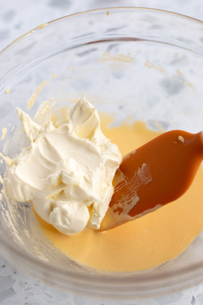 Mascarpone cream being added to a bowl of creamed egg yolks and sugar, preparing the filling for classic tiramisu.