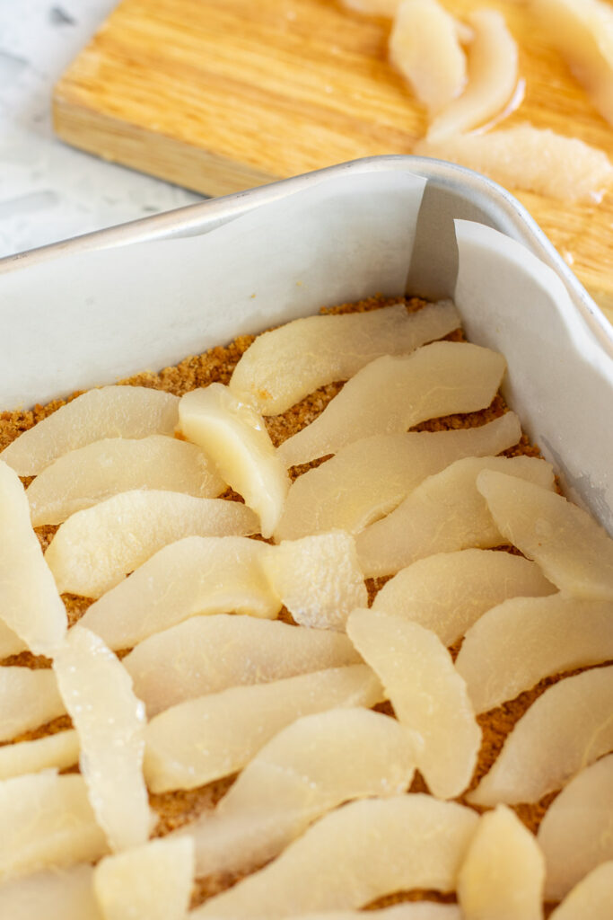 Pear slices neatly arranged over the biscuit base, with extra slices on a cutting board in the background.