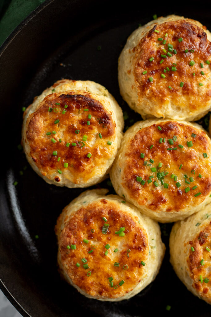 Top-down view of cheddar chive buttermilk biscuits in a cast iron skillet, fresh out of the oven. 