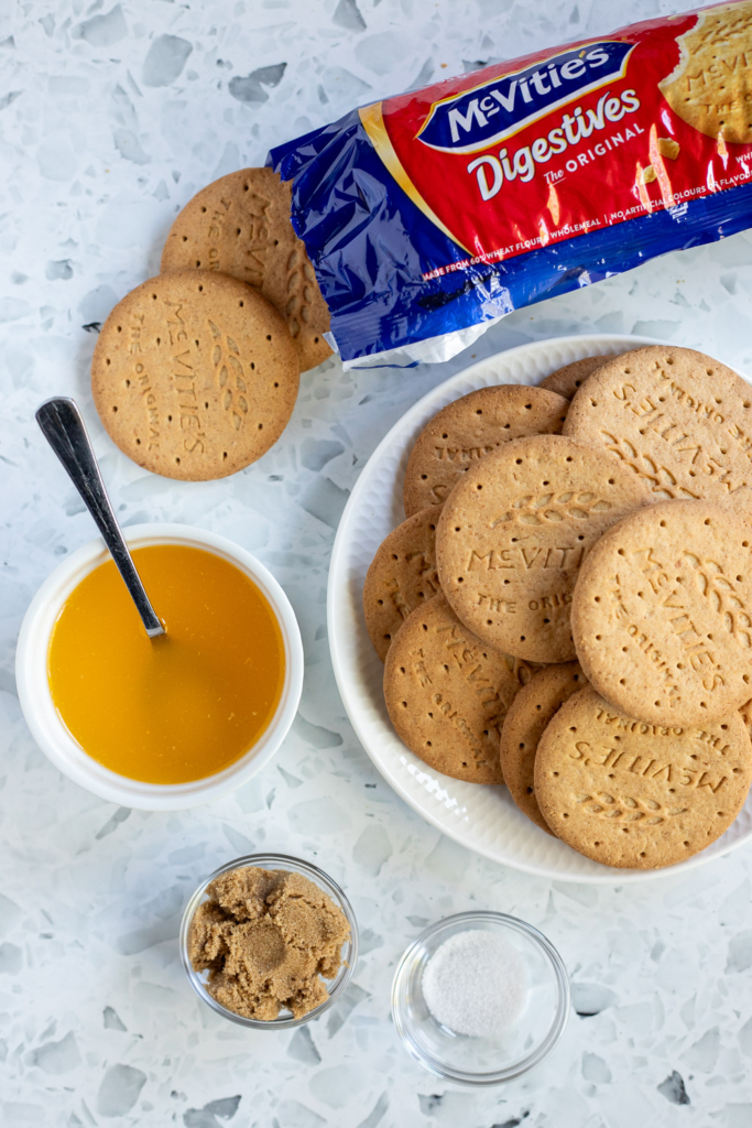 Flat lay of ingredients for the biscuit base and crumble topping — digestive biscuits, brown sugar and melted butter.