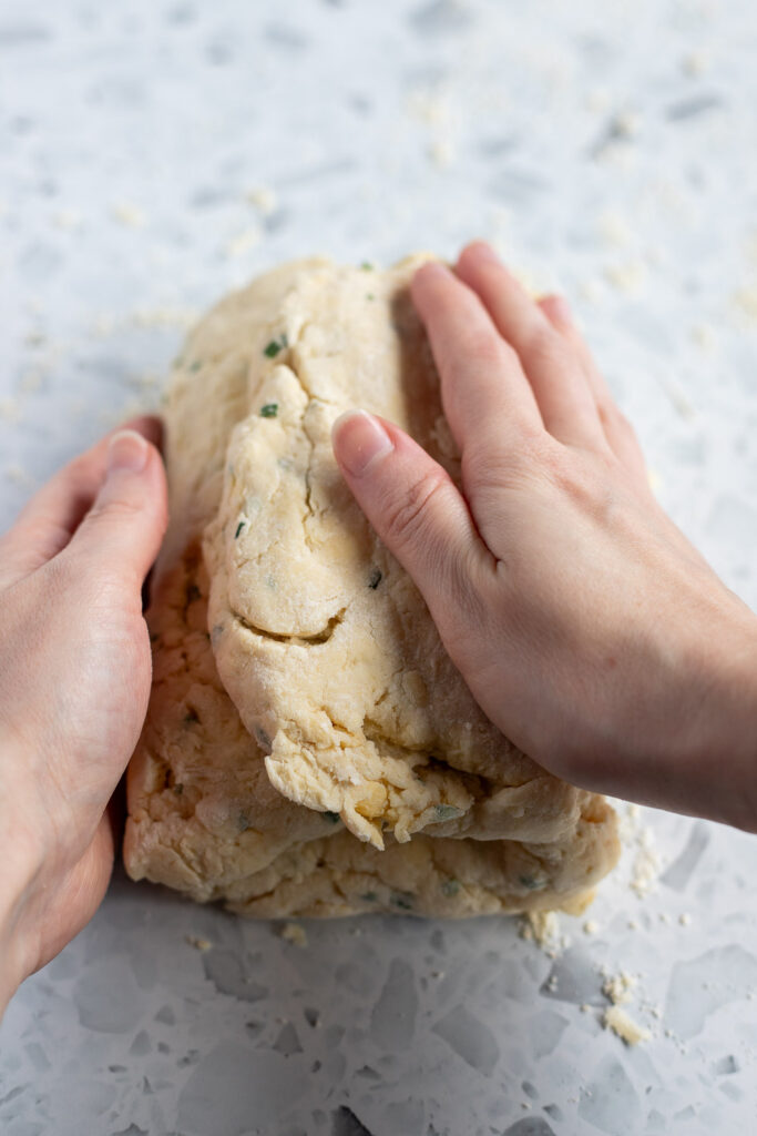 Hands folding biscuit dough into thirds like a letter, creating layers for flaky biscuits.