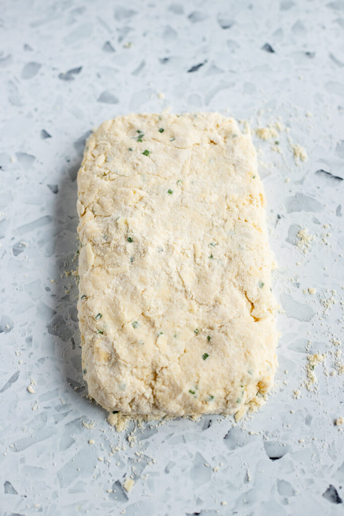Biscuit dough on a floured countertop, patted into a rectangle.