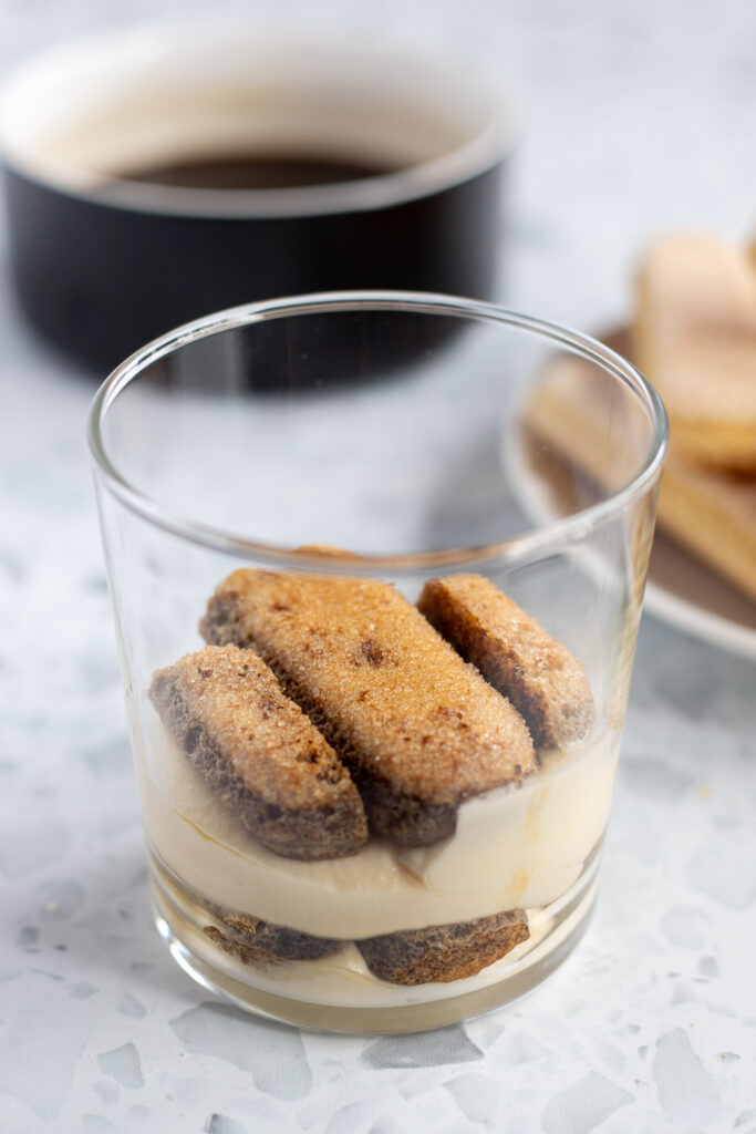 Close-up showing the next layer of coffee-soaked ladyfingers being added