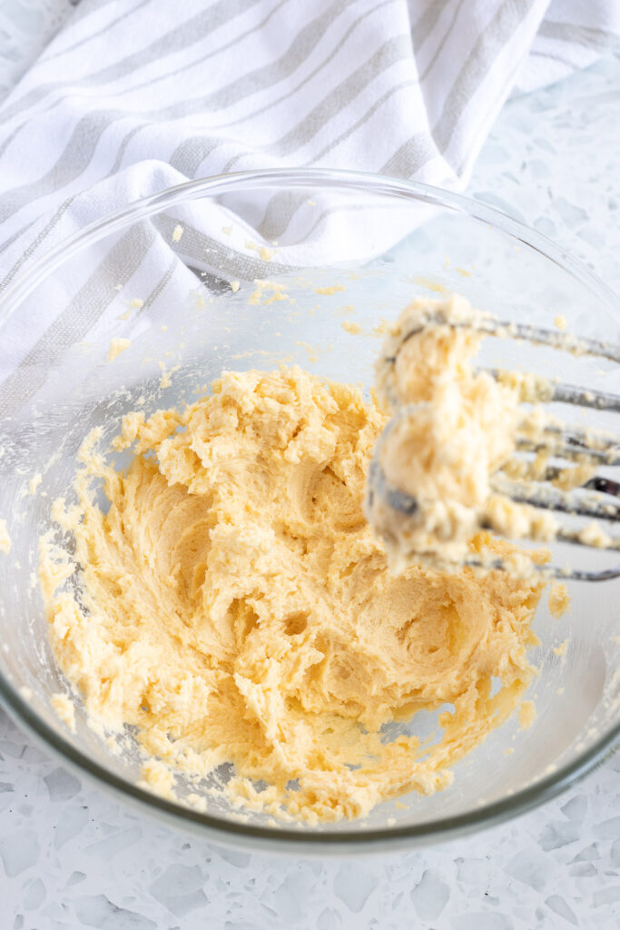 Butter and sugar creamed together in a large mixing bowl, with whisk attachments resting above the rim. 