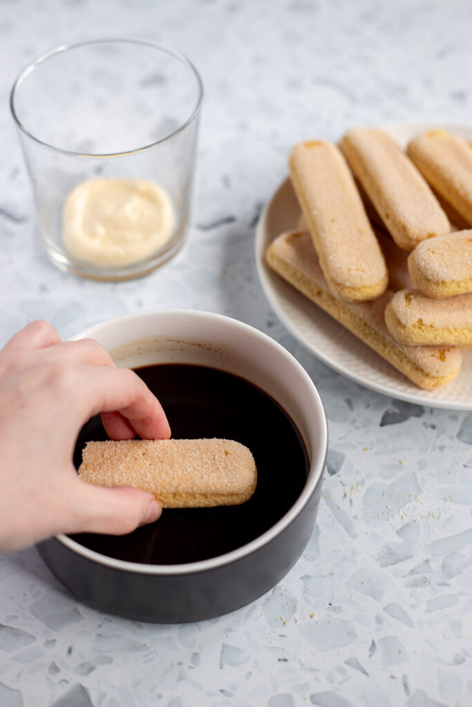 Hand dipping a broken ladyfinger into coffee soak.