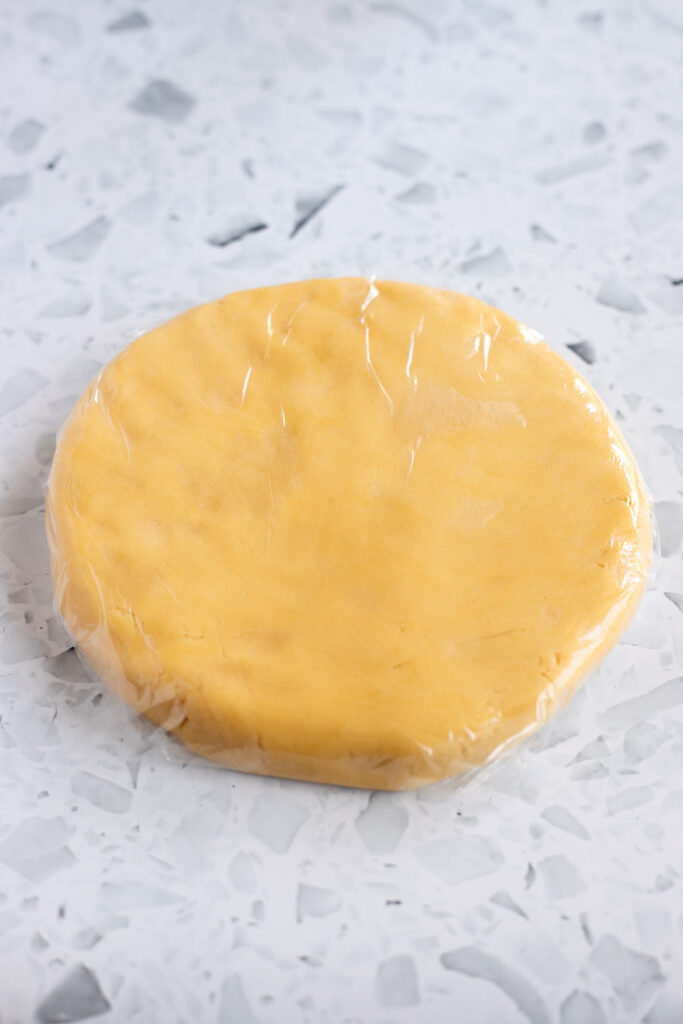 Shortbread dough flattened into a disc and wrapped tightly in cling film, ready for chilling.