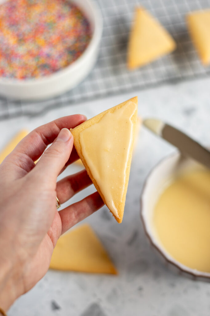 Hand holding a shortbread cookie coated in a thin layer of butter icing, ready for decorating.