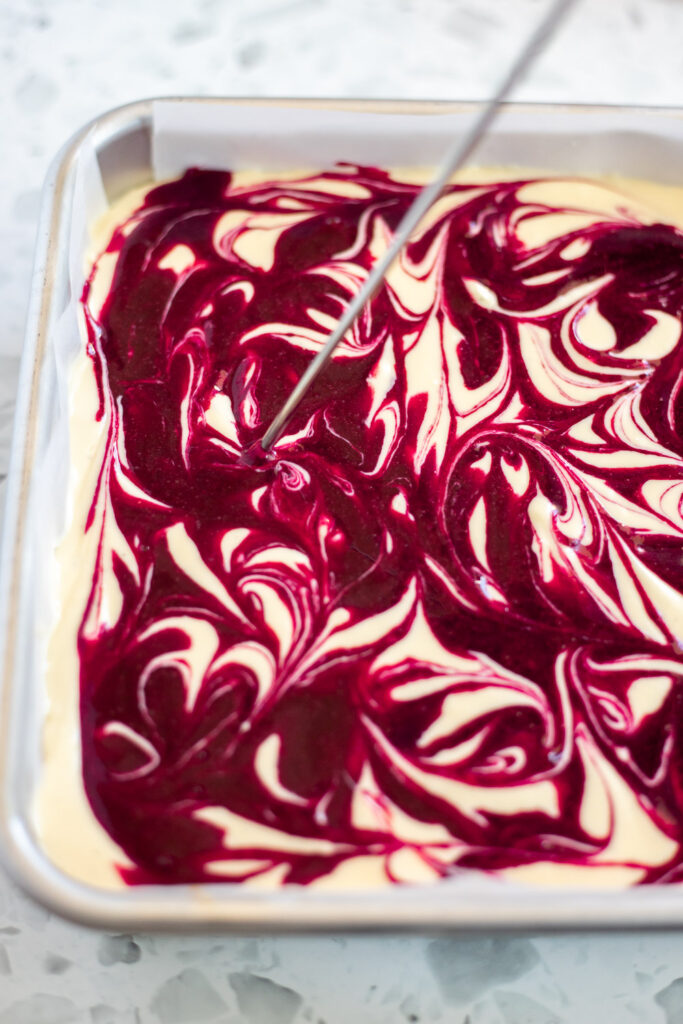 Using a metal skewer to swirl blackberry sauce into the cheesecake filling, creating a marbled effect.