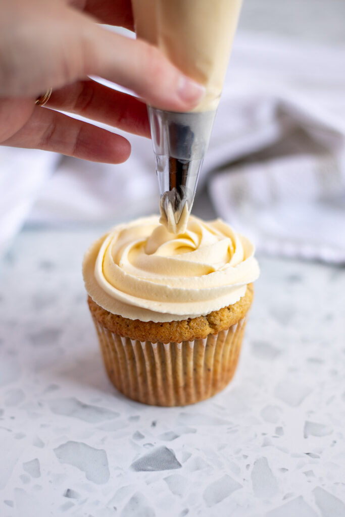 Hand piping swirls of honey mascarpone icing onto cupcake using a piping bag and metal star tip. 
