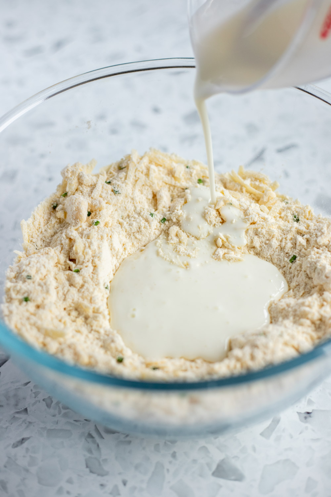 Buttermilk being slowly poured into a well in the centre of the flour mixture.
