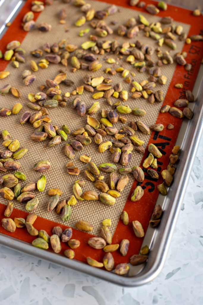 Roasted pistachios evenly spread out on a baking tray lined with a silicone mat. 