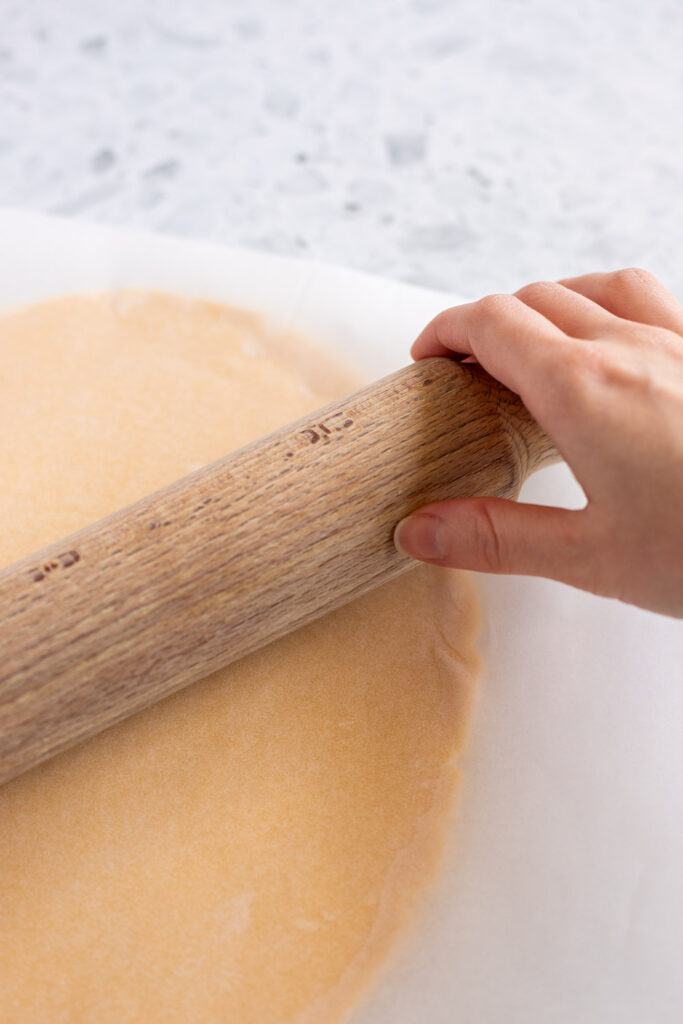 Rolling shortbread dough between two sheets of parchment paper, using a rolling pin for even thickness.