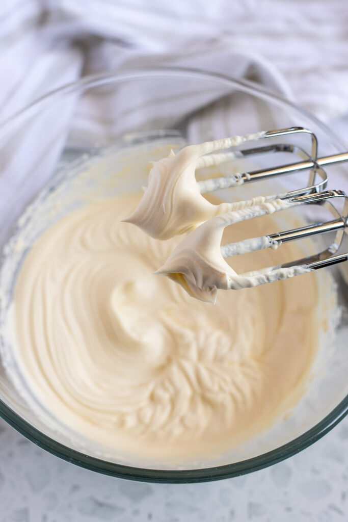Whipped honey mascarpone icing beaten to stiff peaks in a bowl, ready to pipe onto pistachio cupcakes.