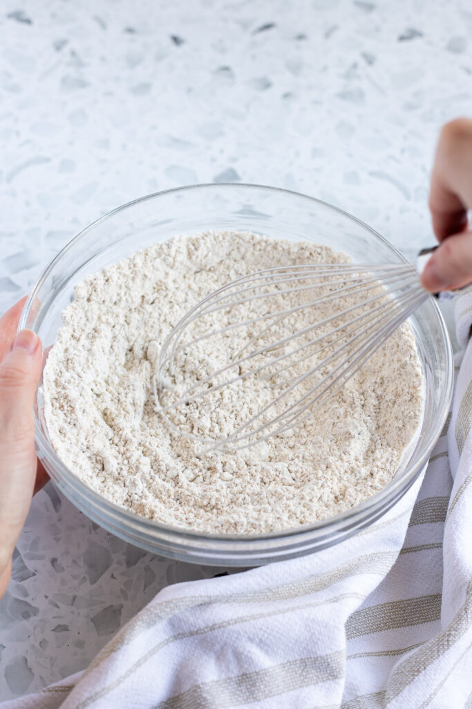 Hand whisking together dry ingredients for cupcakes in a glass mixing bowl. 