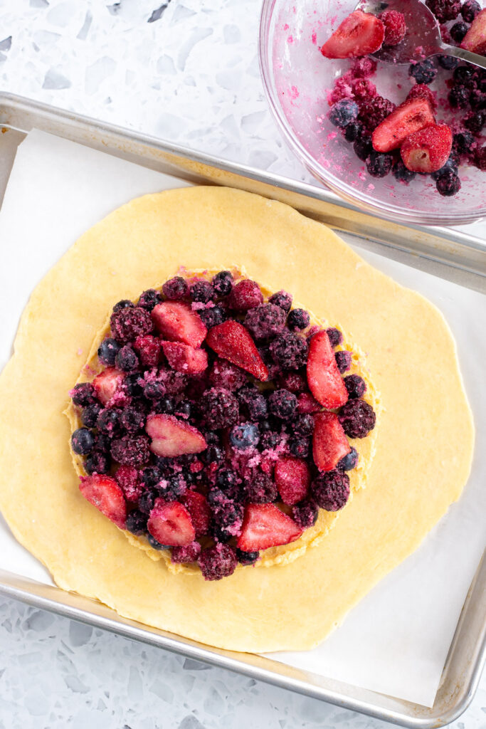 Berry filling placed on top of frangipane in the center of galette dough, with a bowl of extra berry filling in the background.