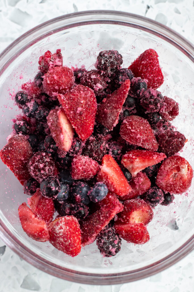 Close-up of frozen mixed berries coated in sugar, cornflour, and vanilla for galette filling. 