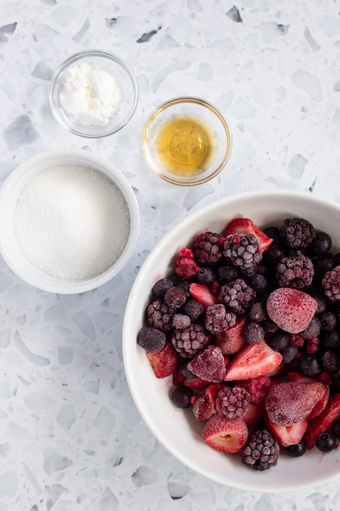 Flatlay of ingredients for mixed berry filling, featuring frozen berries, sugar, and cornflour.