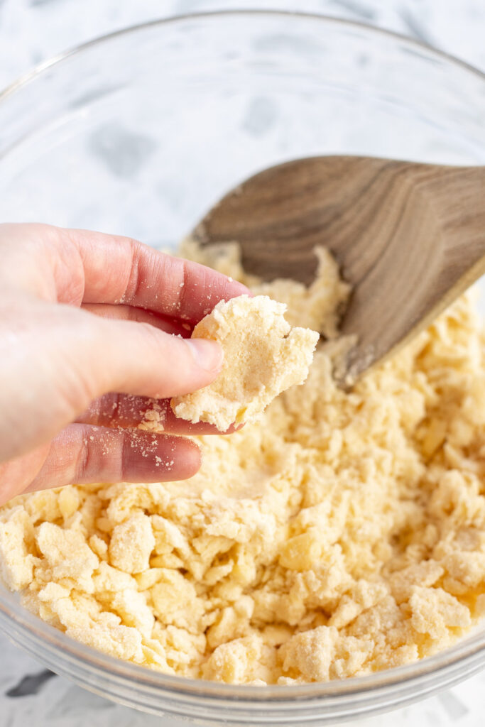 Hand squeezing a piece of pastry dough between fingers to check if it has enough moisture.
