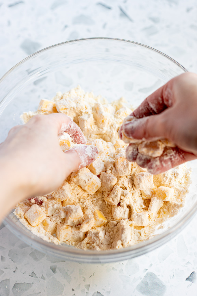 Hands working cold butter into flour to make a flaky pastry dough.