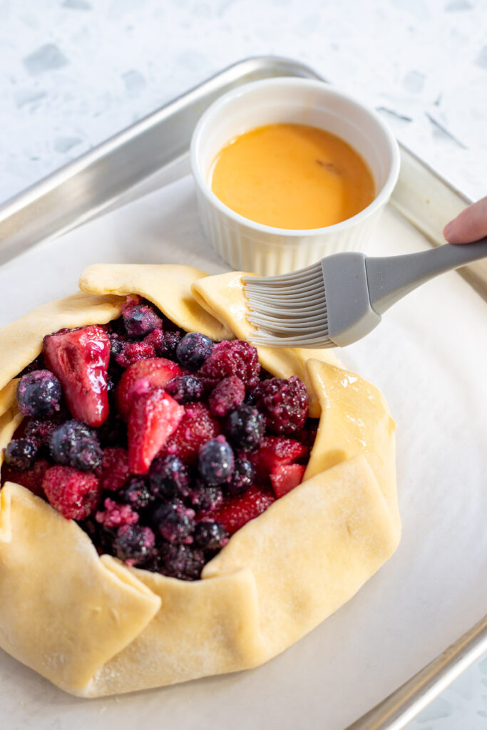Close-up of hand applying egg wash to galette dough with a silicone pastry brush before baking.