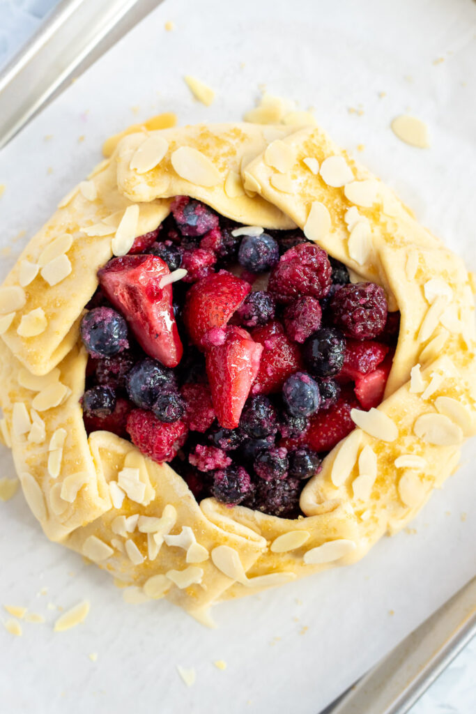 Overhead shot of a ready-to-bake mixed berry frangipane galette topped with coarse sugar and flaked almonds.