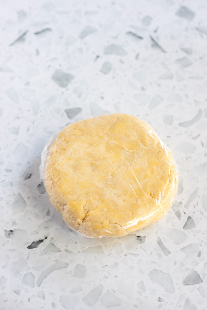 Galette pastry dough flattened into a disc and wrapped in cling film, ready to be chilled.