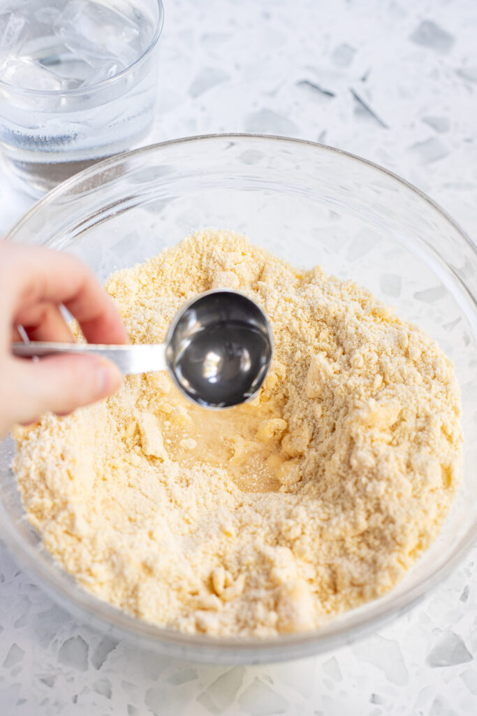 Hand adding ice water one tablespoon at a time to hydrate the pastry dough.