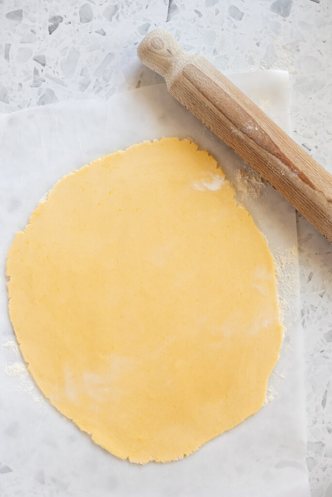 Overhead shot of rolled-out lemon shortbread dough with a wooden rolling pin to the side, ready for cutting.