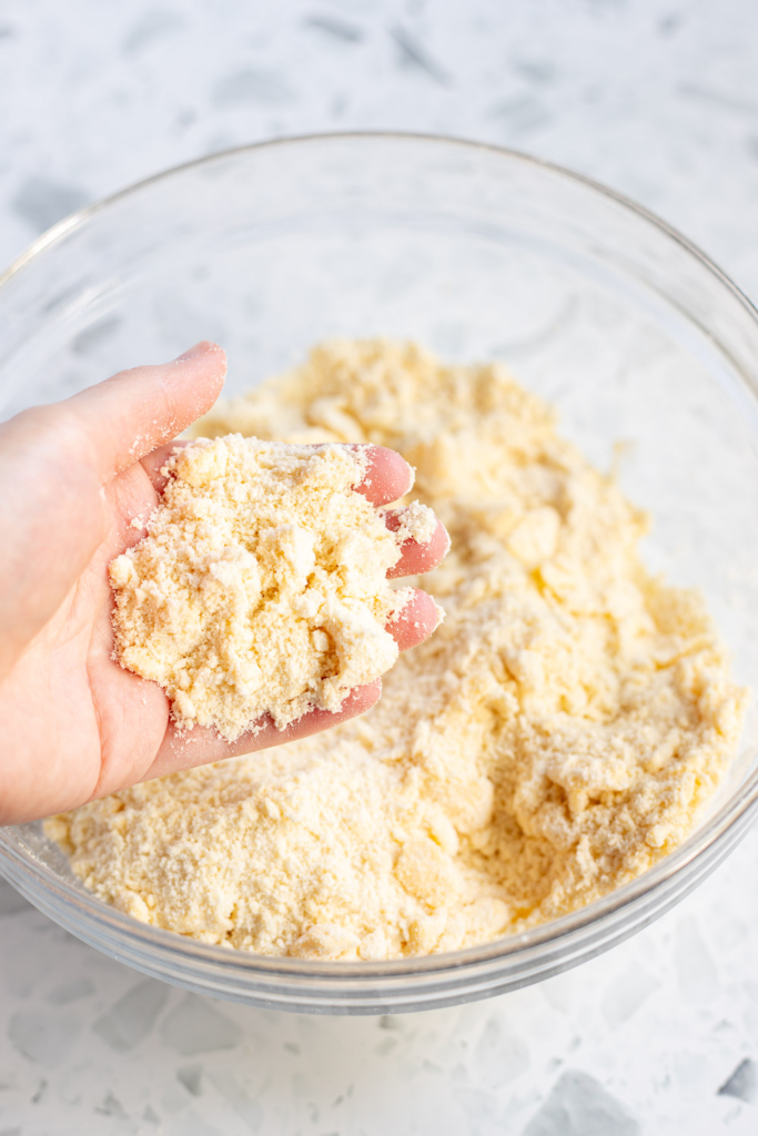 Hand displaying coarse flour and butter mixture with pea-sized pieces of butter. 