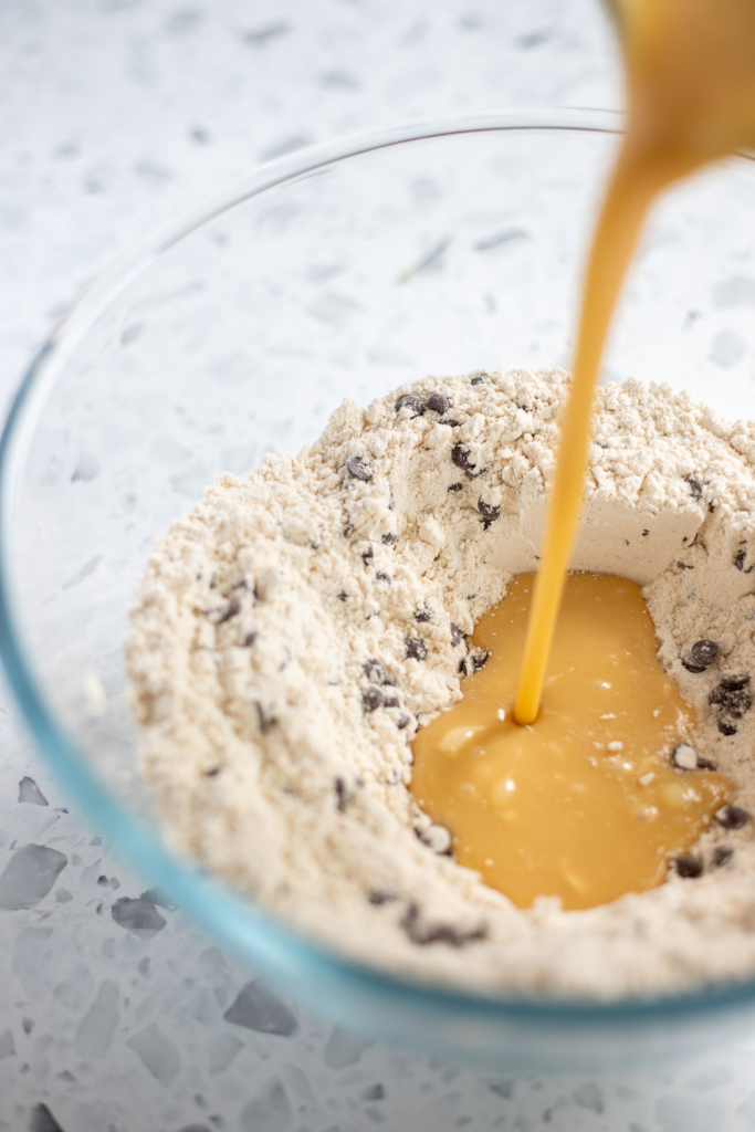Close-up action shot of wet ingredients being poured into dry ingredients to make chocolate chip muffin batter.