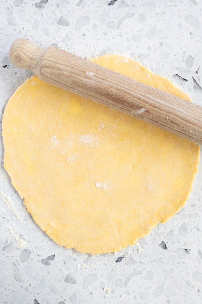 Overhead shot of galette dough rolled into a circle with a wooden rolling pin on top, ready for filling.