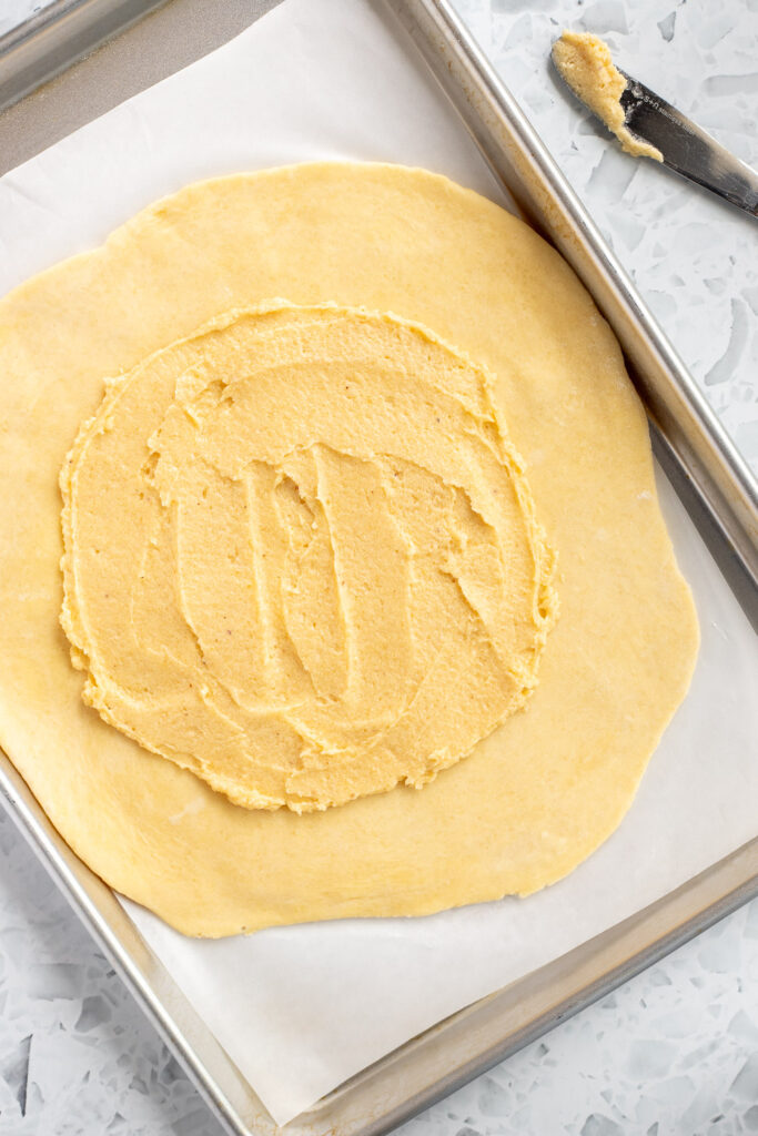 Overhead shot of galette dough on a baking sheet, frangipane spread in the center with a clear border for folding the edges.