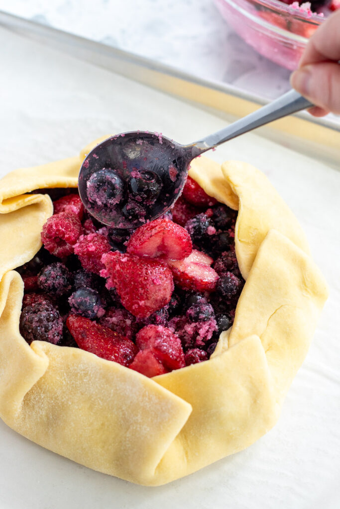 Close-up of hand adding the rest of the mixed berry filling to the center of a galette.