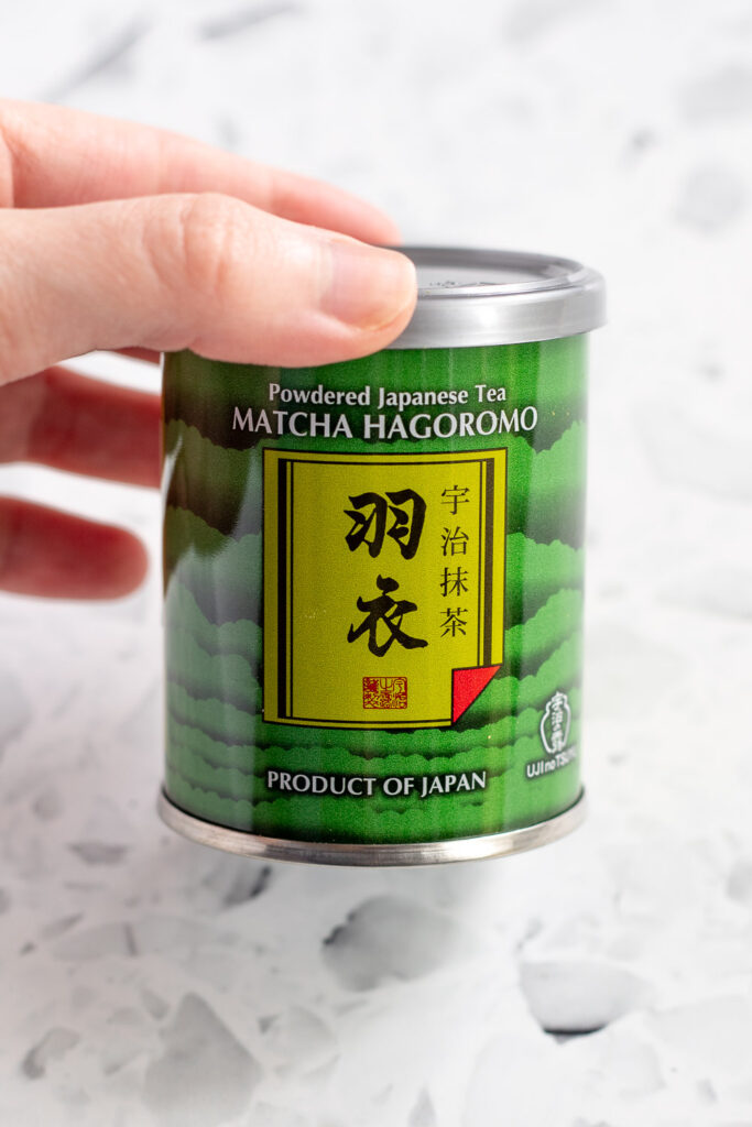 Close-up of a hand holding a small tin of Japanese matcha powder.