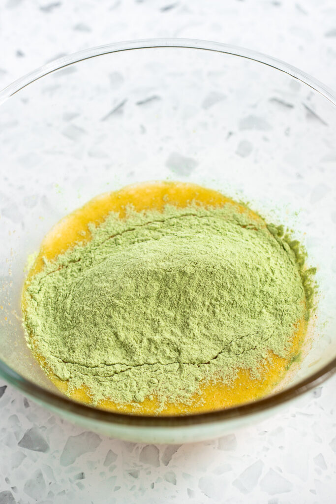 Egg yolk mixture in a bowl with dry ingredients on top, ready to be mixed.