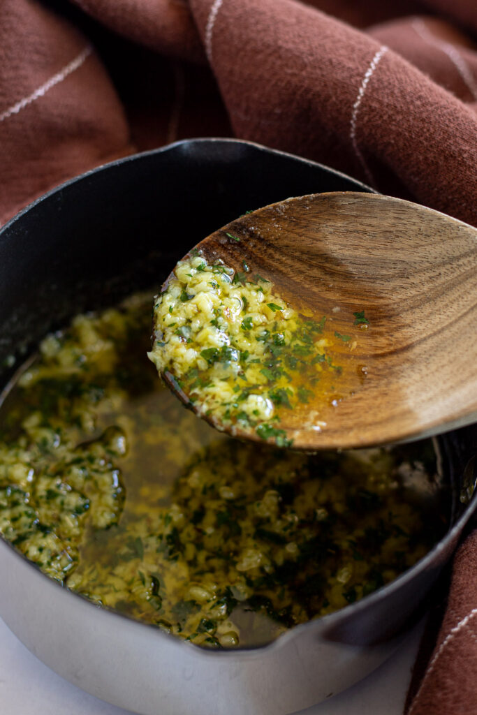 Melted garlic butter on a spoon above a saucepan, ready for brushing.