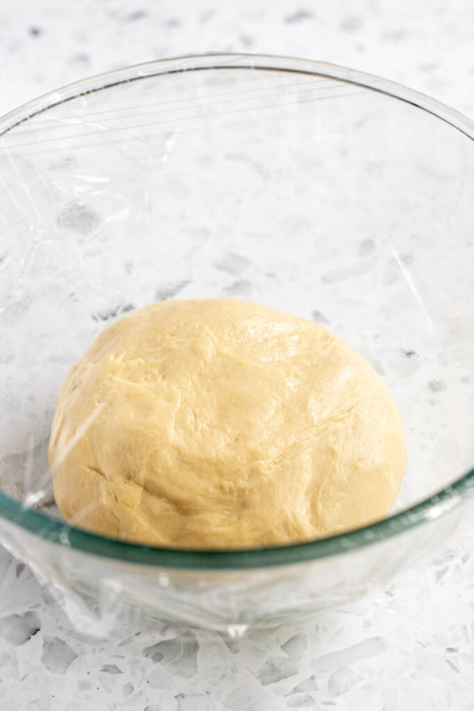Oiled glass bowl with garlic knot dough under cling film, ready for its first rise.