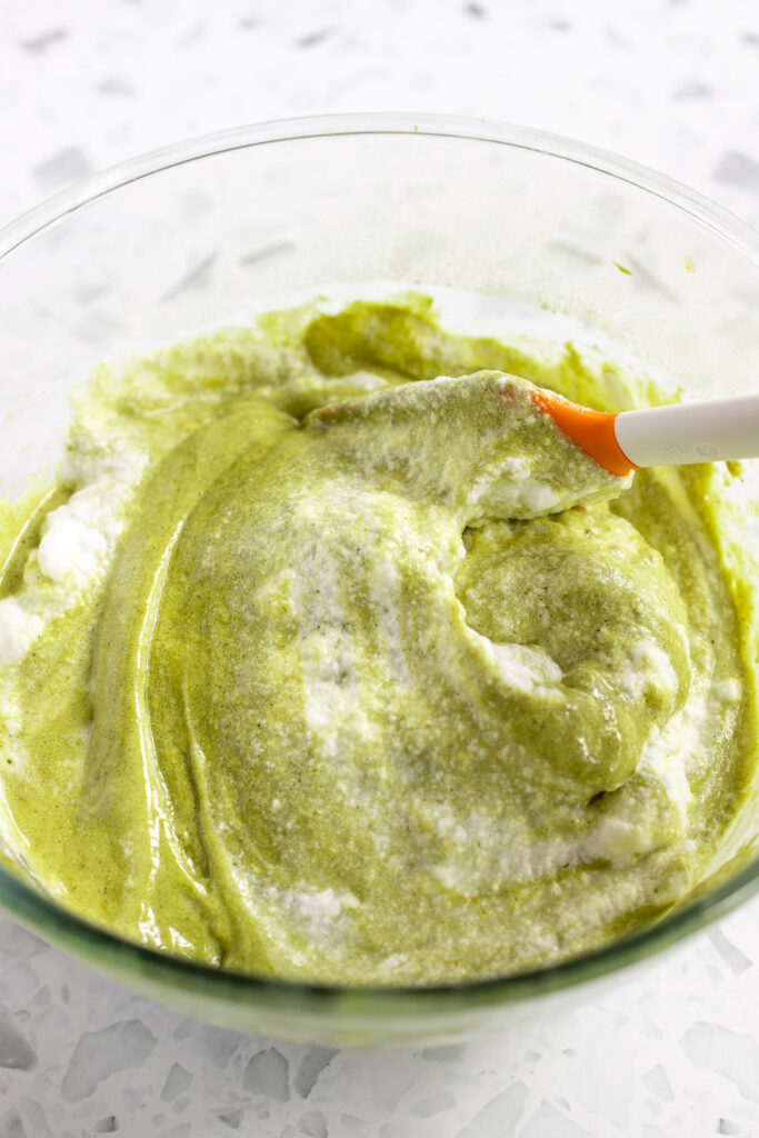 Egg whites being folded into matcha cake batter with a rubber spatula.