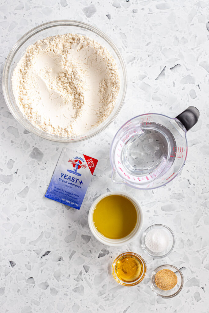 Top-down view of ingredients for homemade garlic knot pizza dough, including bread flour, instant yeast, and garlic powder.