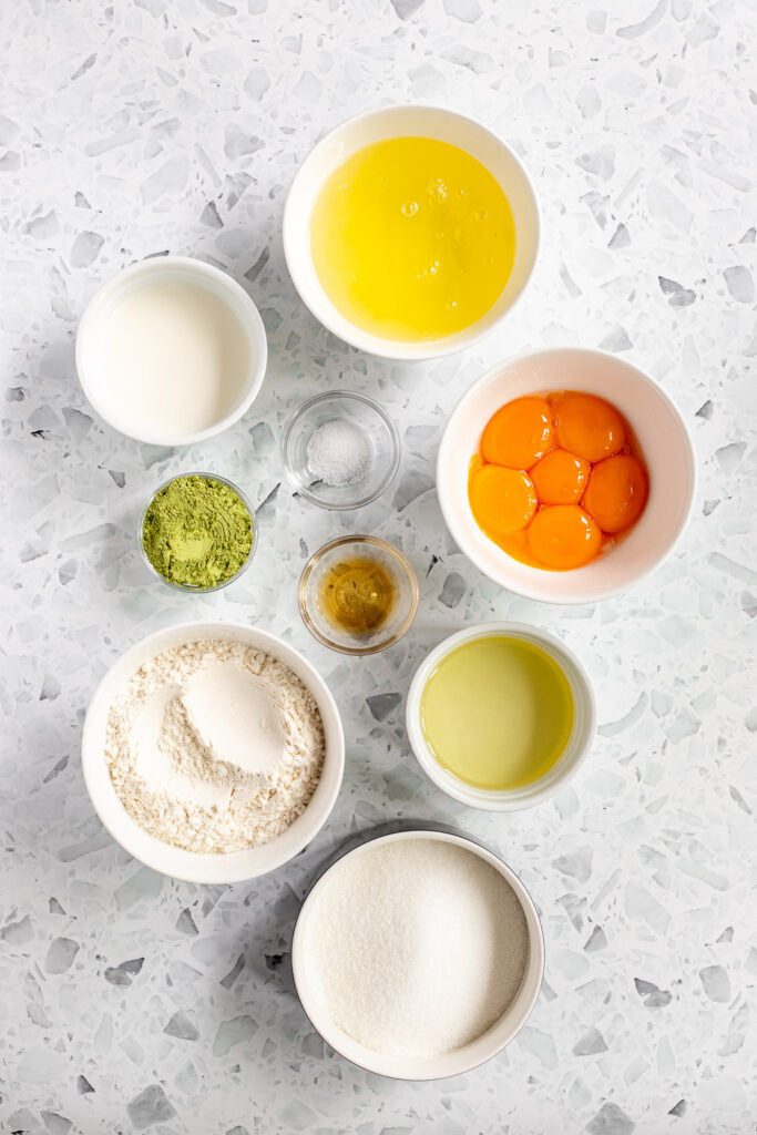 Flat lay of ingredients for making matcha sponge, including egg yolks, egg whites, matcha powder, and other baking essentials.
