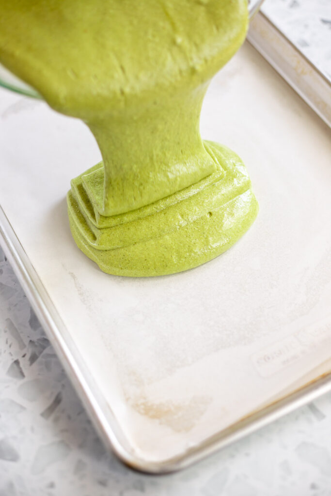 Action shot of green matcha batter being poured into a lined baking tray.
