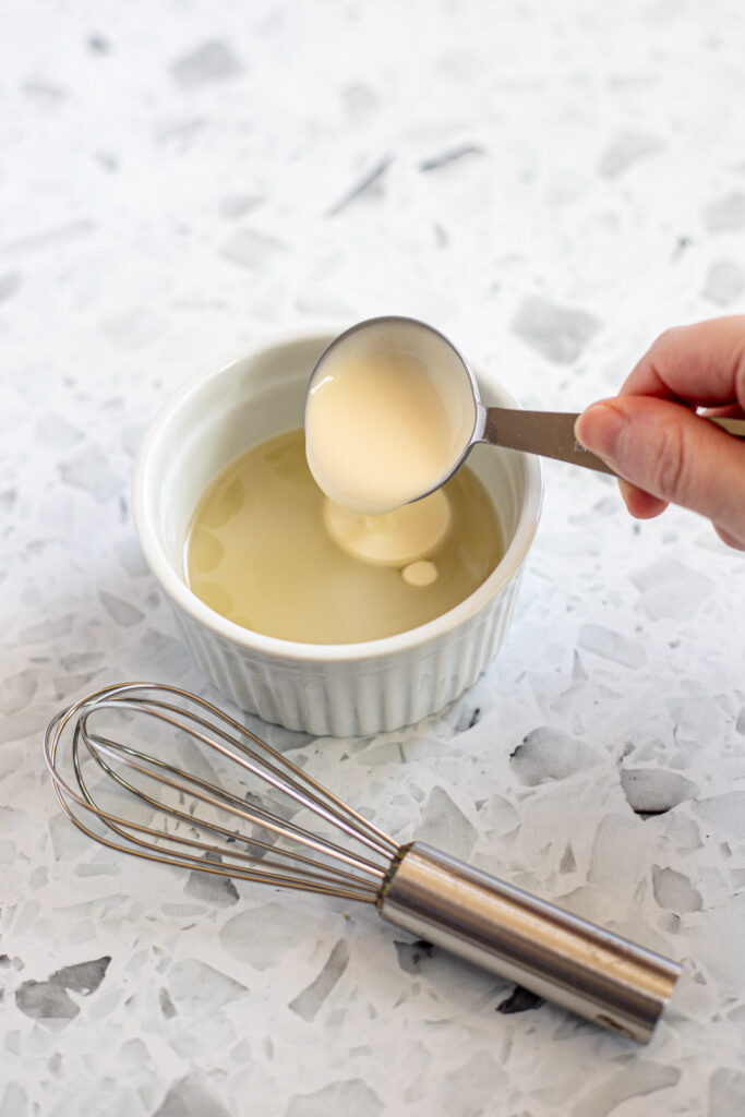 Cream being mixed with melted gelatine in a small ramekin for stabilised cake filling.
