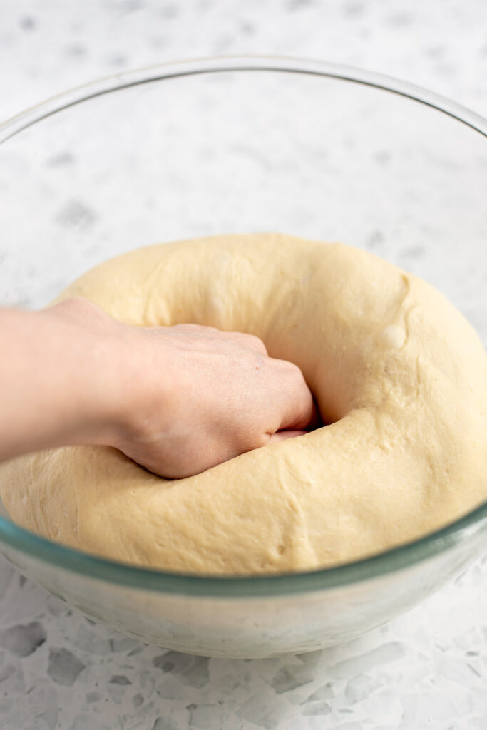 Hand gently punching down garlic knot dough to release air bubbles.