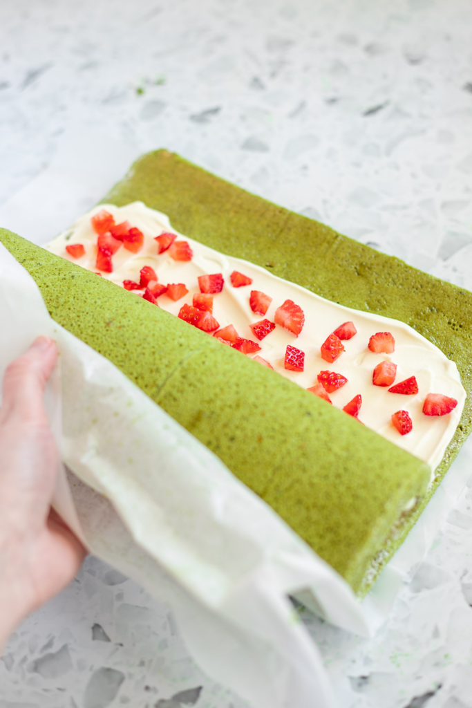 Rolling the sponge back up with cream and strawberry filling inside.