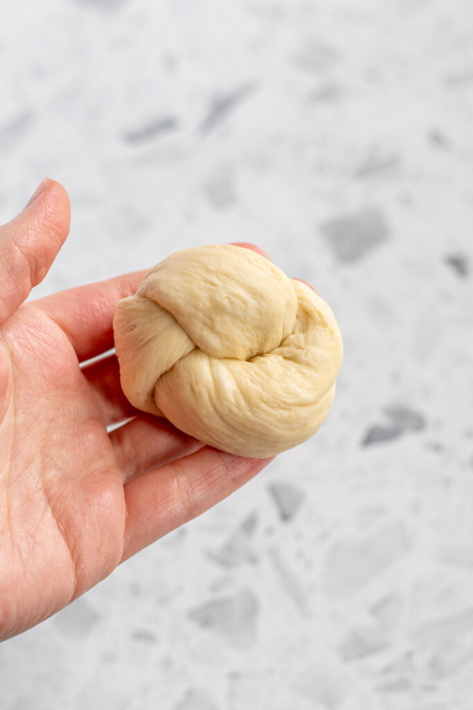 Hand-shaped garlic knot prepared for the baking sheet, with ends tucked underneath.